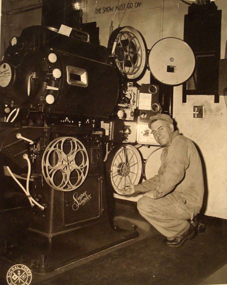 A projectionist kneeling beside a restored 35mm projector